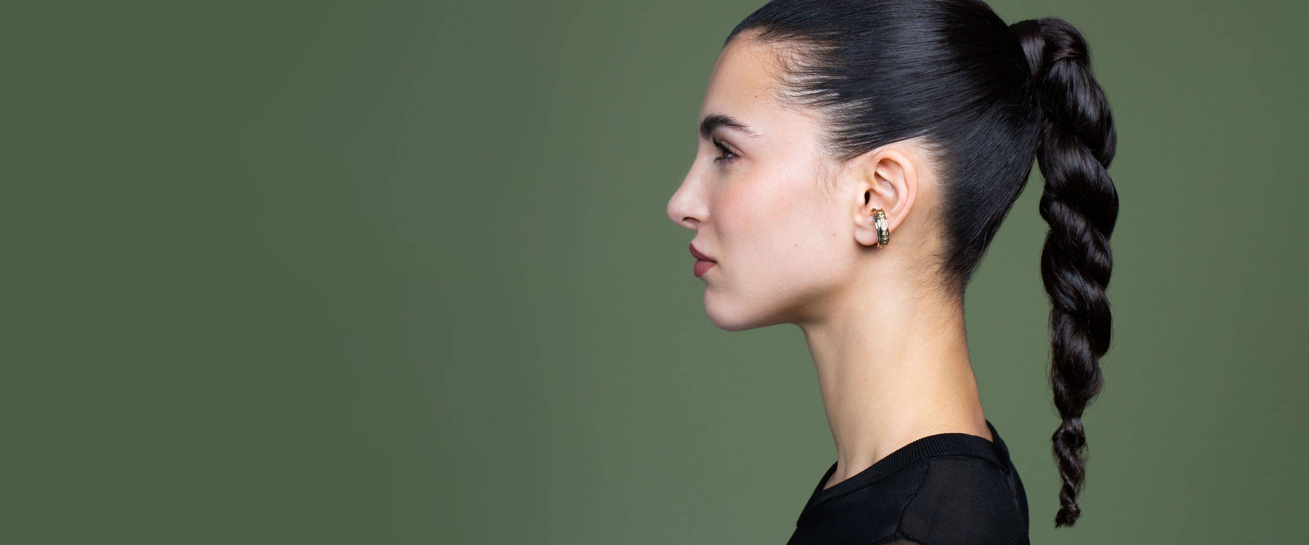 Femme de profil aux cheveux tirés et nattés sur l'arrière et portant un bijou d'oreille strassé dans l'oreille