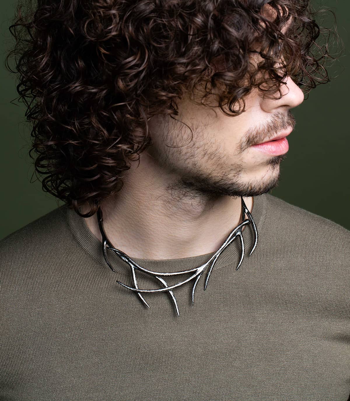 Homme dont la tête est tourné, portant sur son pull un collier ruthénium inspiré de la forme des branches.