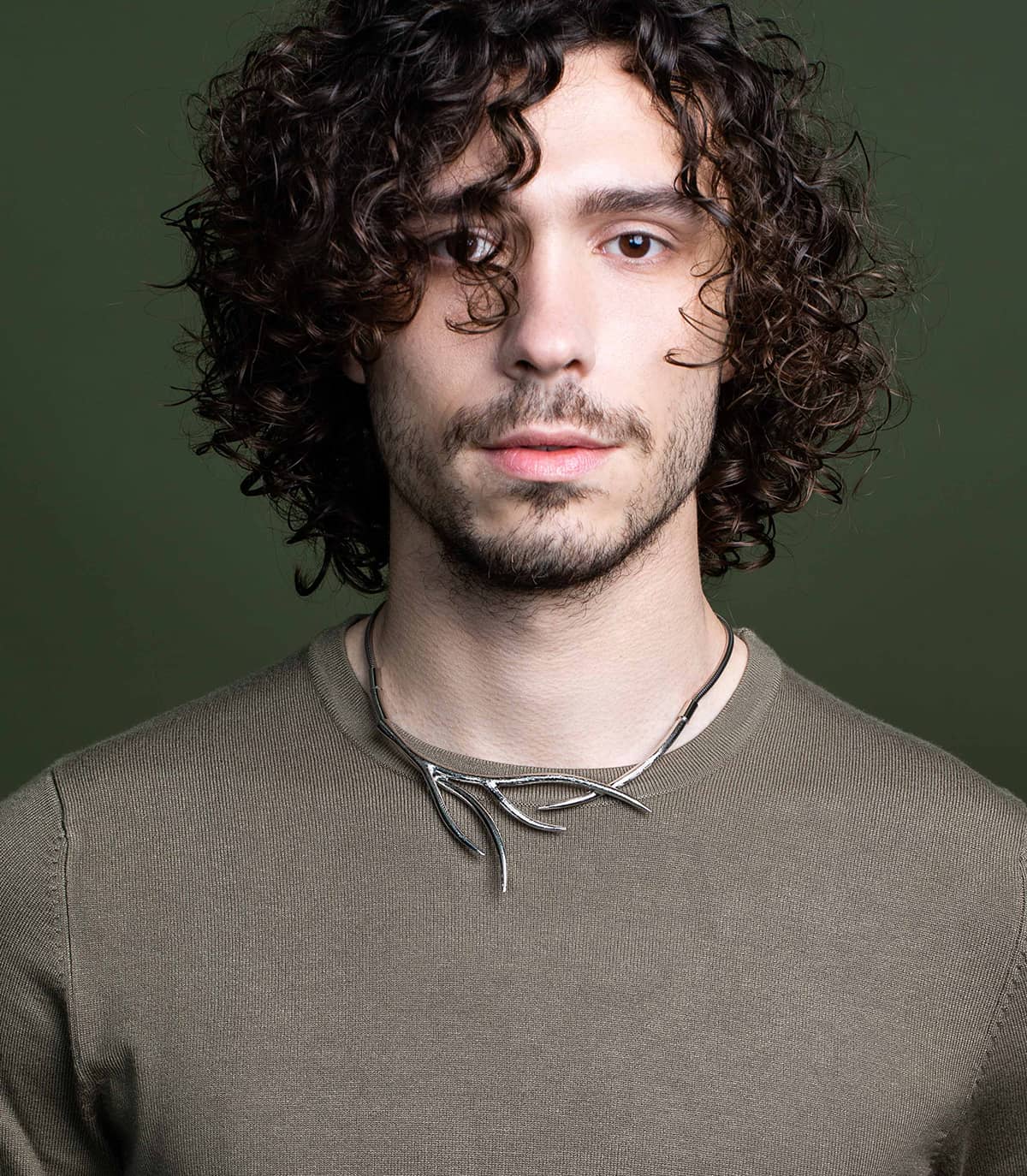 Homme portant sur son pull un collier ras de cou argenté inspiré de la forme des branches.