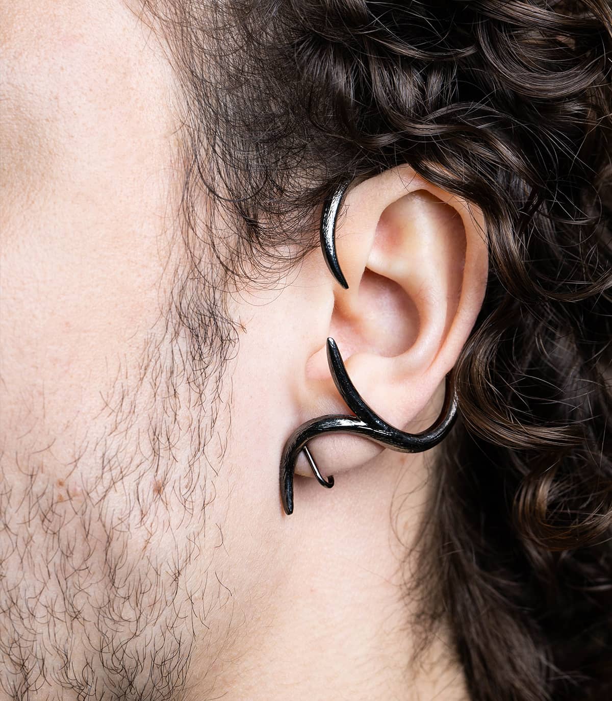 Zoom sur l'oreille d'un homme portant un bijou d'oreille ruthénium autour de l'oreille, inspiré de la forme d'une branche.