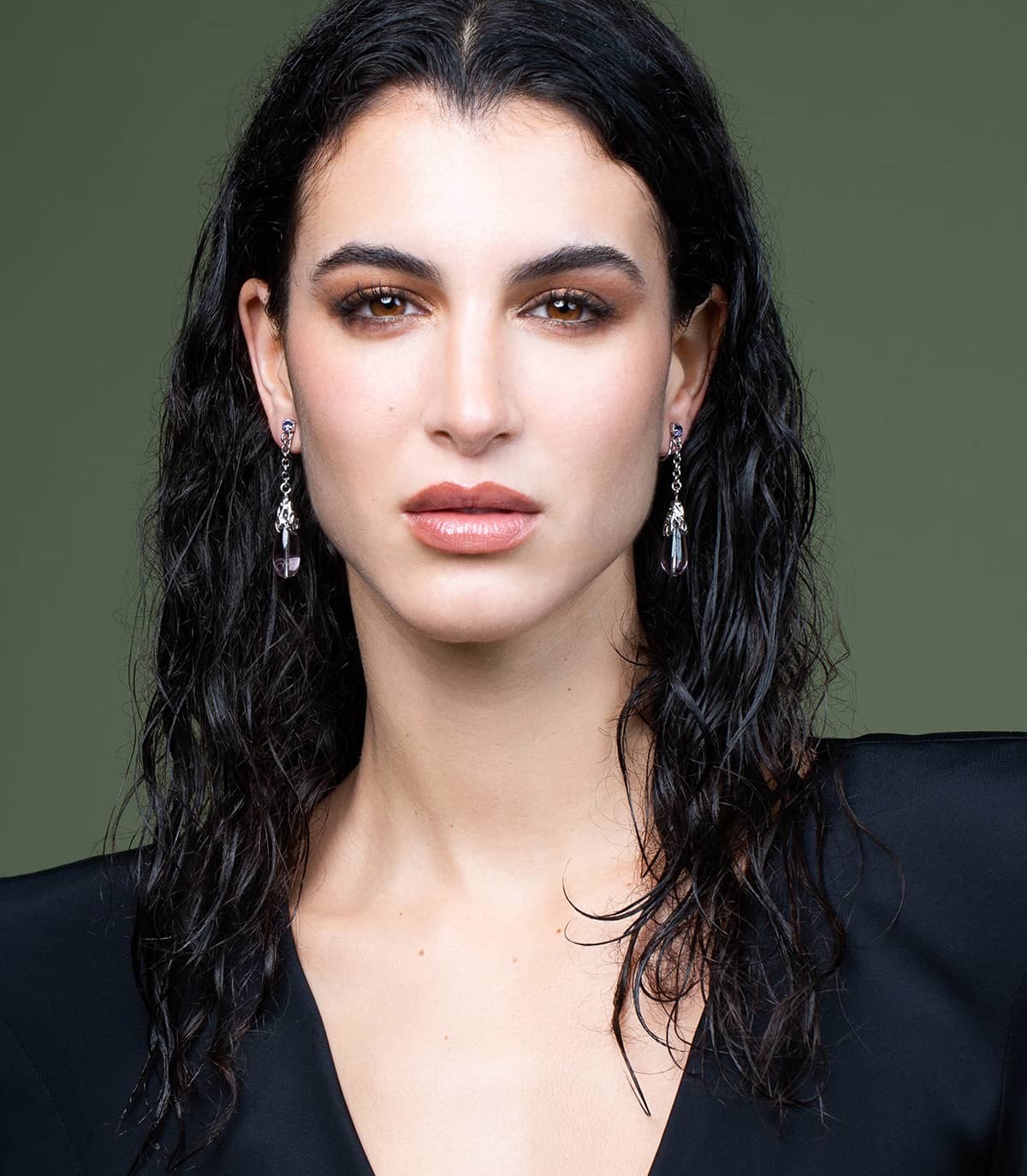 Visage d'une femme portant des boucles d'oreilles argentées en forme de goutte, ornées de perles transparentes mauves.