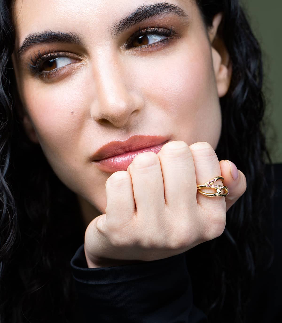 Visage d'une femme se tenant la tête, poing fermé et qui porte à l'index une bague dorée en forme de branches ornée de strass. 