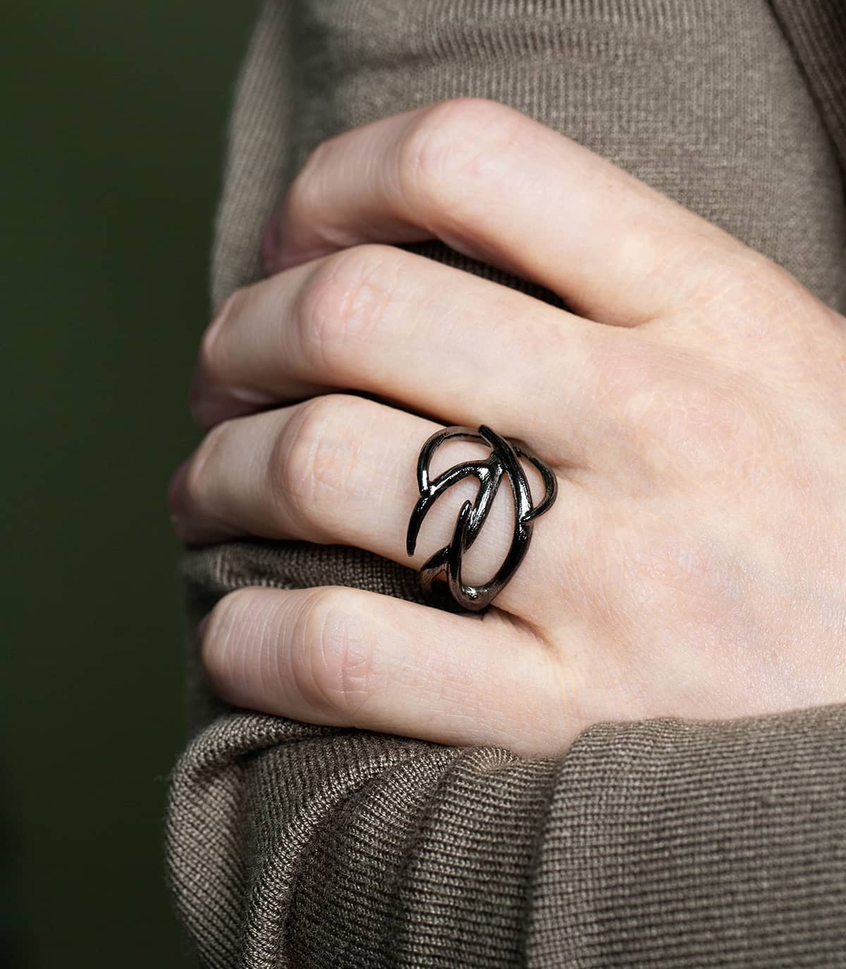 Zoom sur la main d'un homme les bras croisés sur son pull et portant une bague ruthénium en forme de branches.