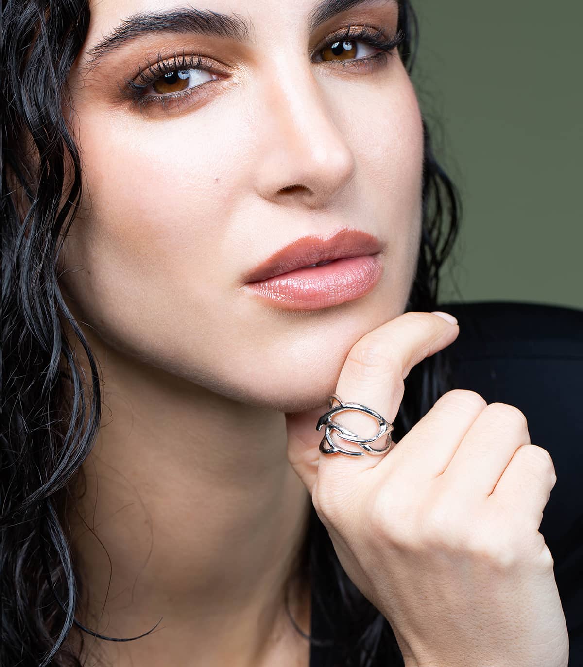 Visage de femme qui se touche le menton et porte au doigt une bague argentée en forme de branches.