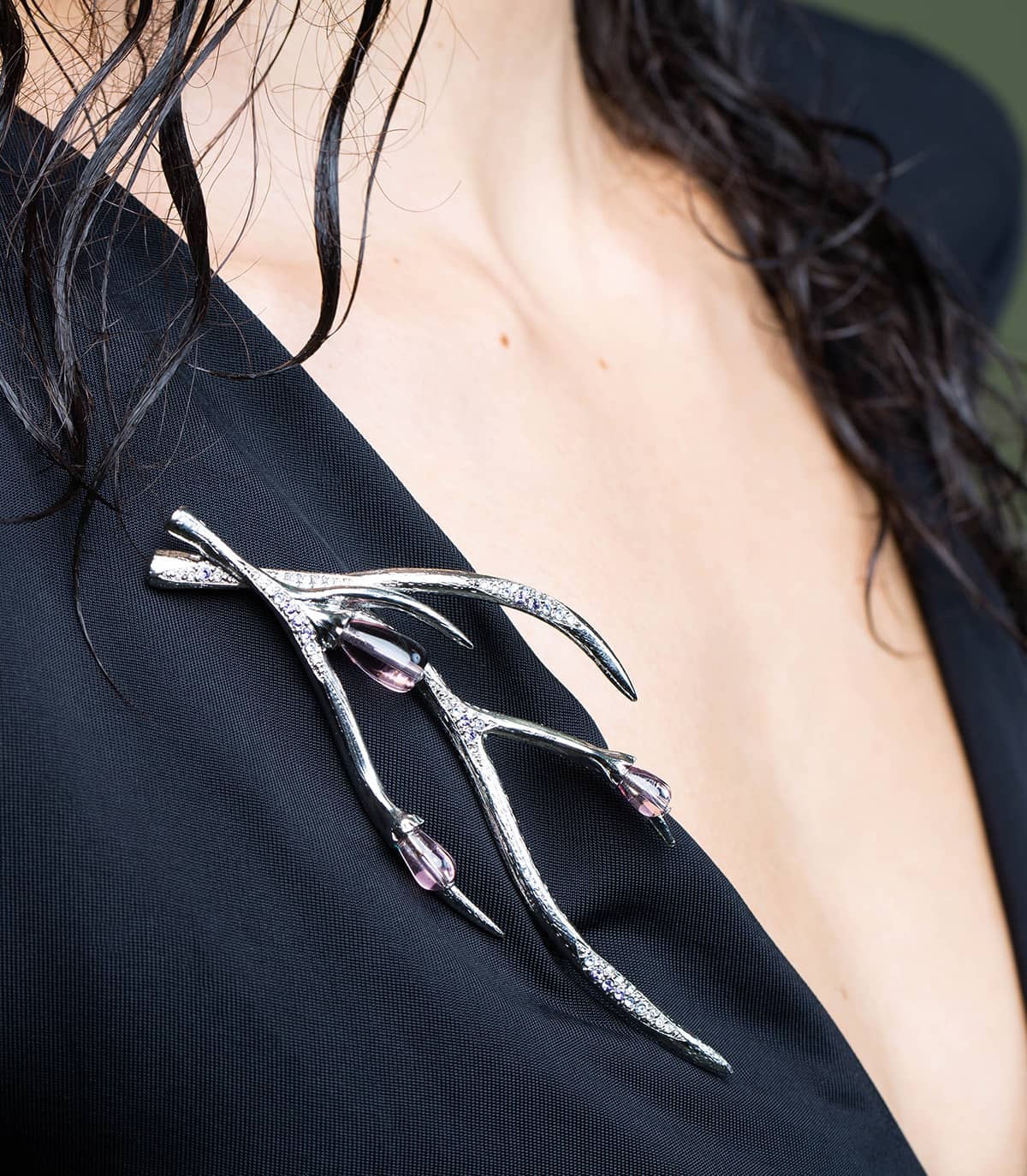 Décolleté d'une femme portant une robe noire et une broche argentée inspirée de la forme des branches, ornée de perles et de strass.