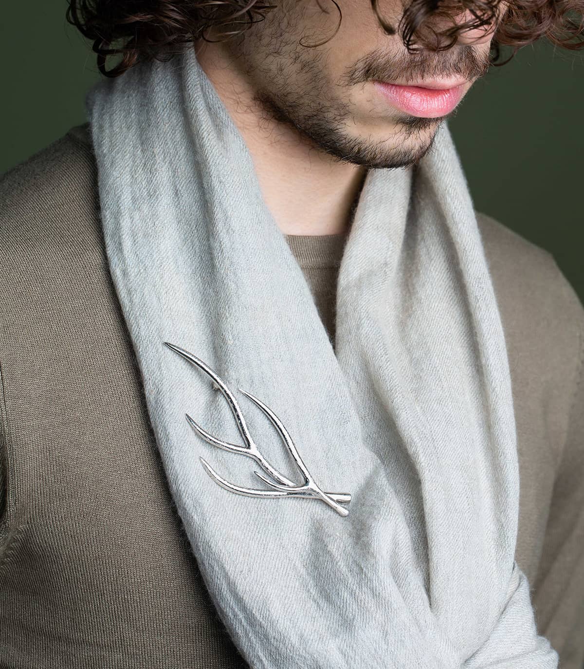 Homme portant une écharpe agrémentée d'une broche argentée inspirée par la forme des branches.