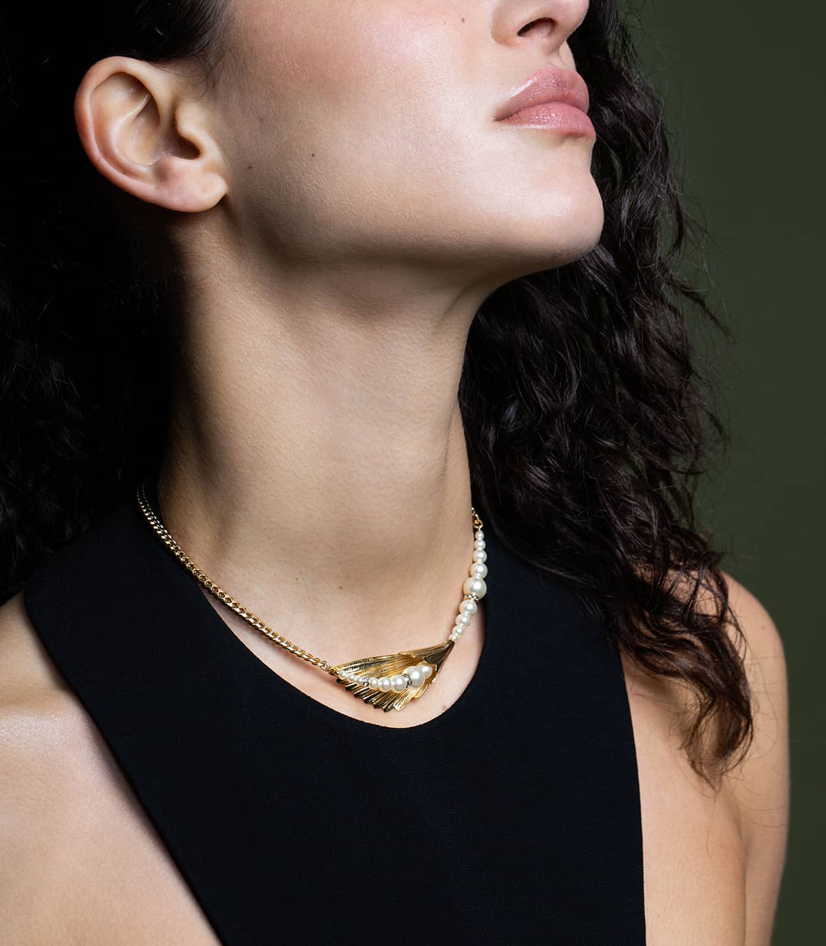 Femme portant une robe noire et un collier ras du cou doré composé d'une feuille, ornée de perles crèmes et terminé par une chaine gourmette.