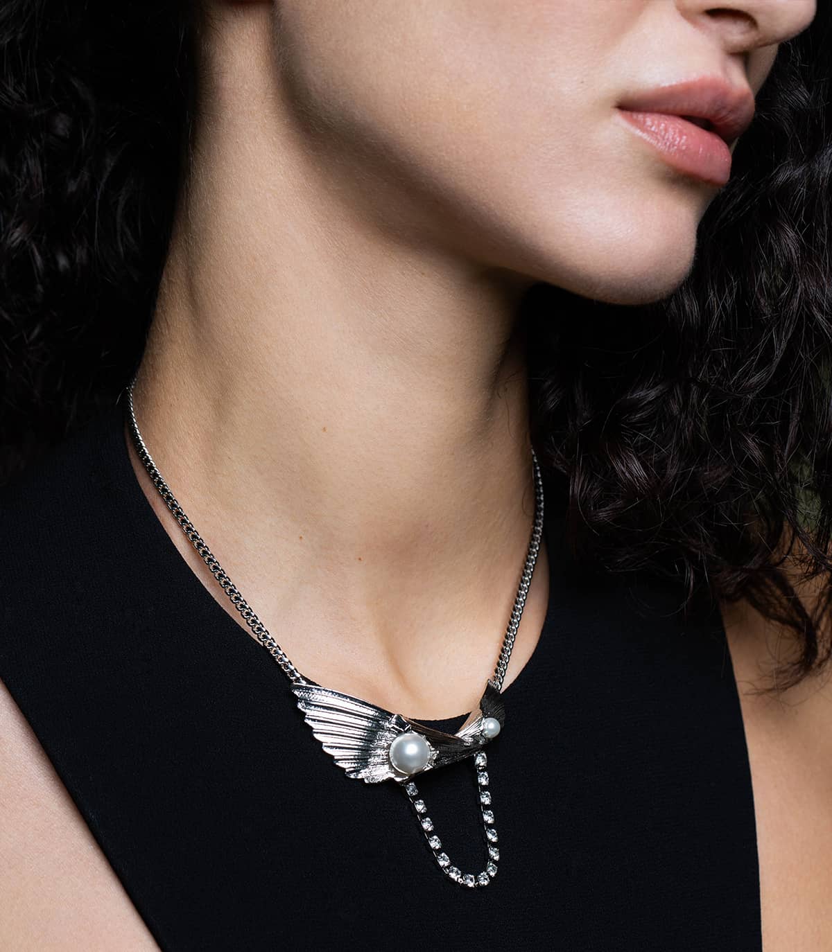 Femme portant un collier argenté composé de deux feuilles, ornées de perles blanches, et d'une chaine strassée et fermé par une chaine gourmette.