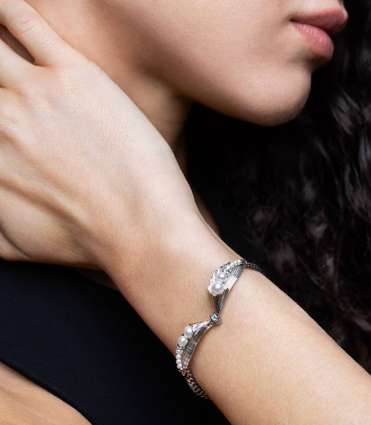 Poignet d'une femme portant un bracelet argenté composé de deux feuilles, ornées de perles blanches, de strass.